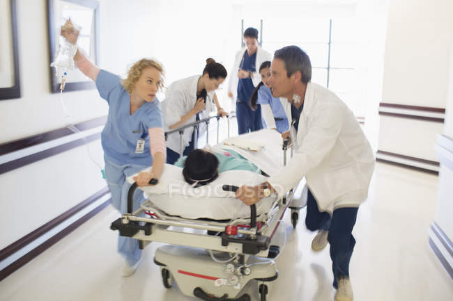 Doctors rushing patient on gurney in hospital corridor — Stock Photo