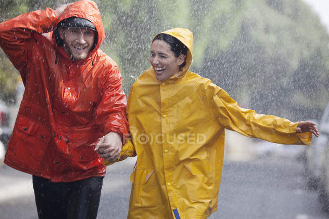 Happy couple holding hands and running in rainy street — Stock Photo