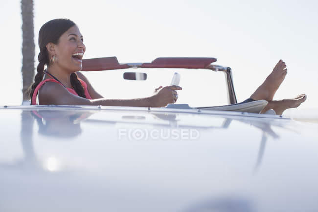 Смеющаяся девушка с помощью мобильного телефона в кабриолете — стоковое фото