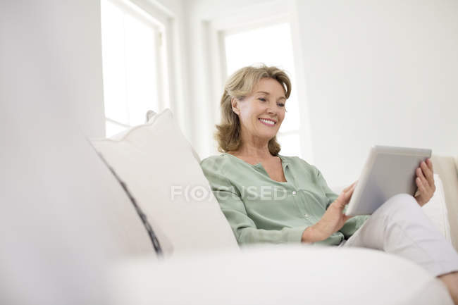 Femme caucasienne senior utilisant une tablette numérique sur un canapé — Photo de stock