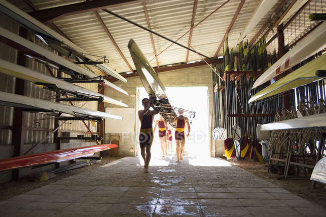 Equipage d'aviron transportant le radeau dans le hangar — Photo de stock