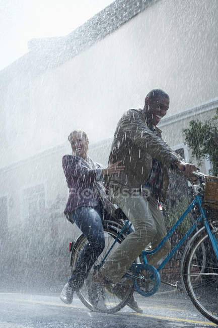 Happy couple riding bicycle in rainy street — Stock Photo