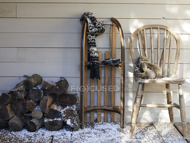 Bufanda, trineo de madera, silla y leña en el porche - foto de stock