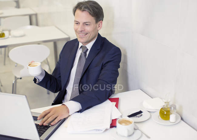 Smiling businessman drinking coffee and using laptop in restaurant — Stock Photo
