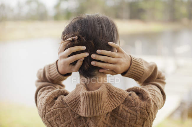 Вид ззаду жінки з волоссям в руках на березі озера — стокове фото