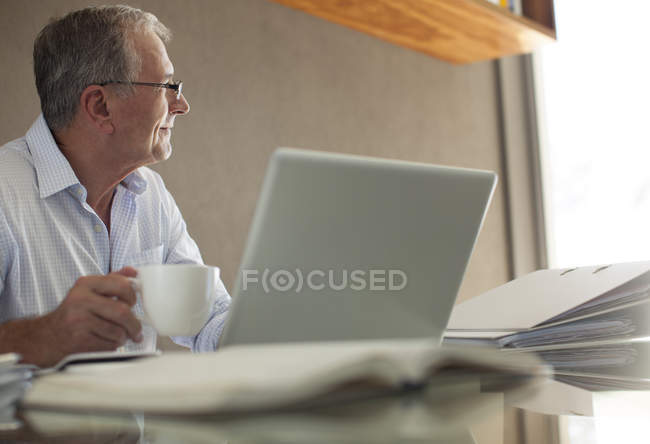 Бизнесмен пьет кофе за ноутбуком — стоковое фото