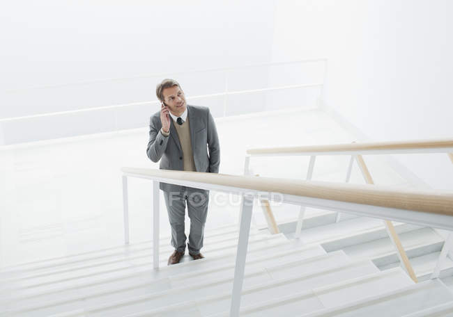 Empresário falando no celular na base das escadas — Fotografia de Stock
