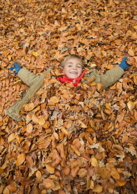 Happy boy laying in autumn leaves — Stock Photo