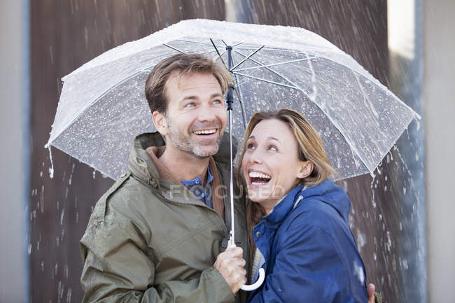 Happy couple under umbrella in downpour — Stock Photo