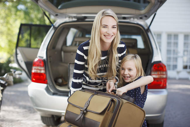 Mother and daughter carrying luggage to car — Stock Photo