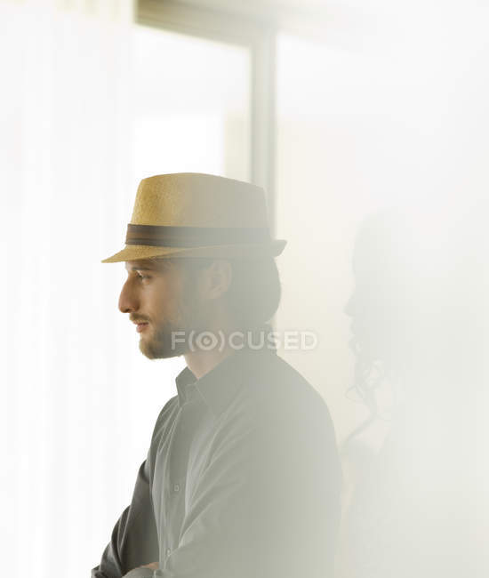 Joven atractivo hombre en sombrero de paja mirando por la ventana - foto de stock