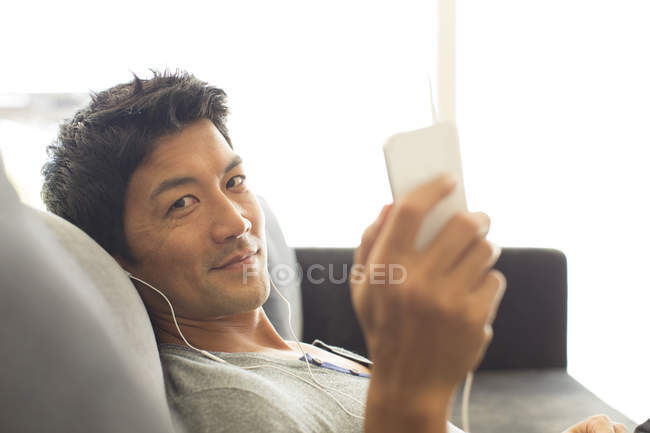 Jeune homme attrayant écoutant des écouteurs sur le canapé — Photo de stock