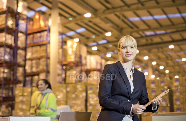 Femme d'affaires utilisant le presse-papiers dans l'entrepôt — Photo de stock