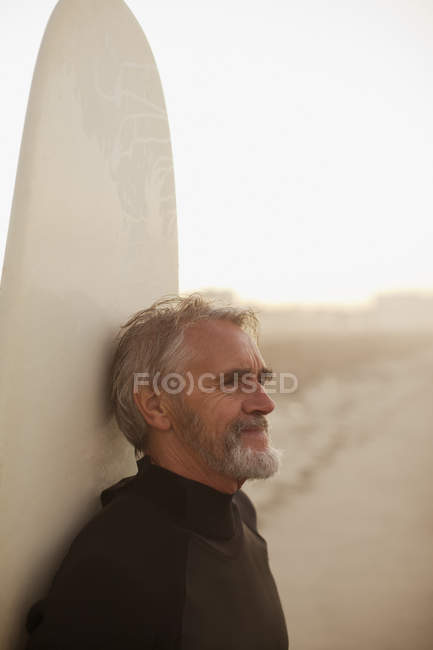 Older surfer leaning on board on beach — Stock Photo