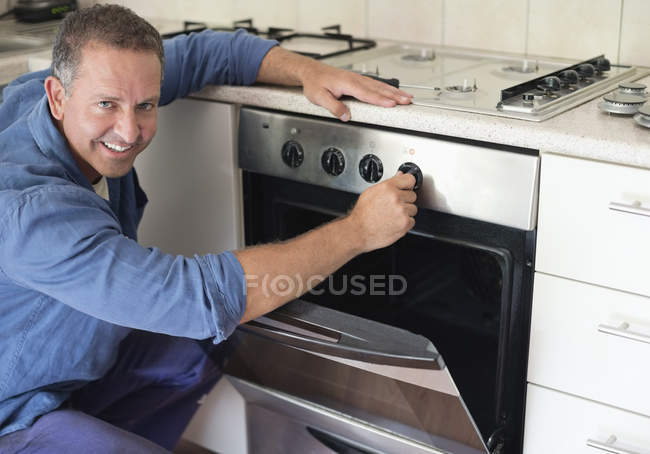 Eletricista caucasiano hábil trabalhando no forno na cozinha — Fotografia de Stock