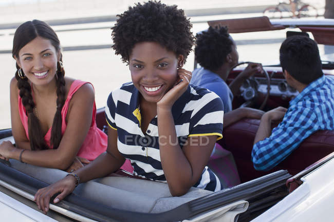 Mujeres sonrientes sentadas en convertibles - foto de stock
