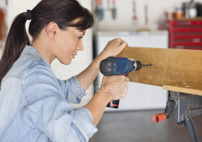 Молодая женщина, работающая с дрелью в мастерской — стоковое фото