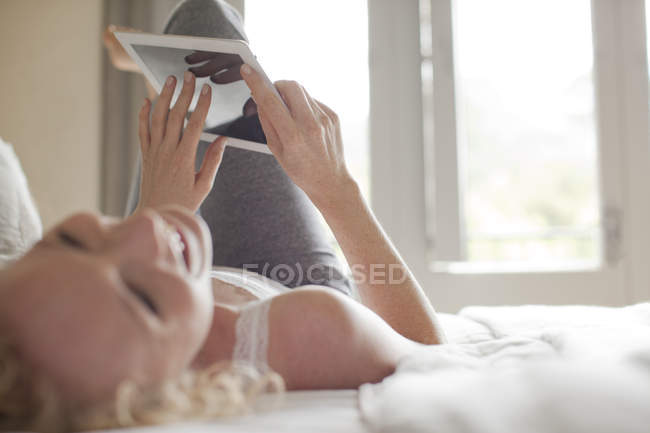Lachende Frau liegt mit digitalem Tablet im Bett — Stockfoto