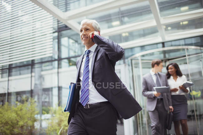 Businessman talking on phone while walking out of office building — Stock Photo