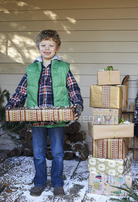 Menino segurando presentes de Natal na varanda nevada — Fotografia de Stock