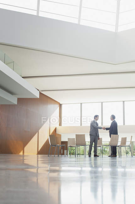 Businessmen shaking hands at circle of chairs in lobby — Stock Photo