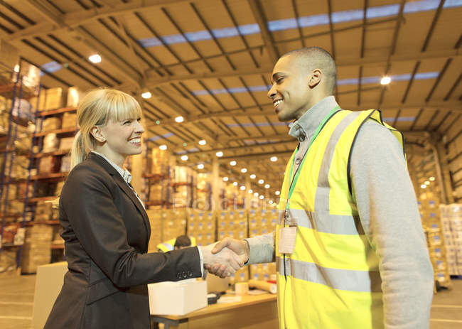 Businesswoman and worker shaking hands in warehouse — Stock Photo