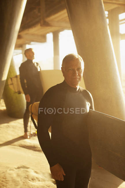 Older surfers carrying boards under pier — Stock Photo