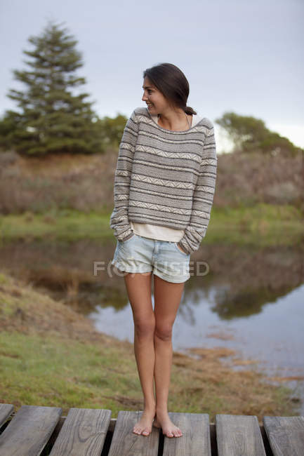 Smiling woman standing on dock with hands in short pockets — Stock Photo