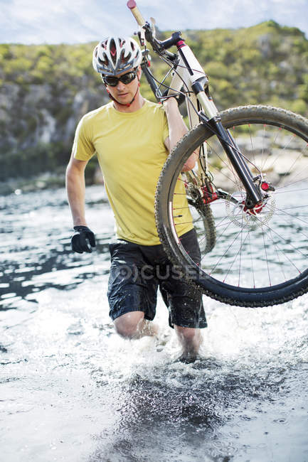 Sporty man carrying mountain bike in river — Stock Photo