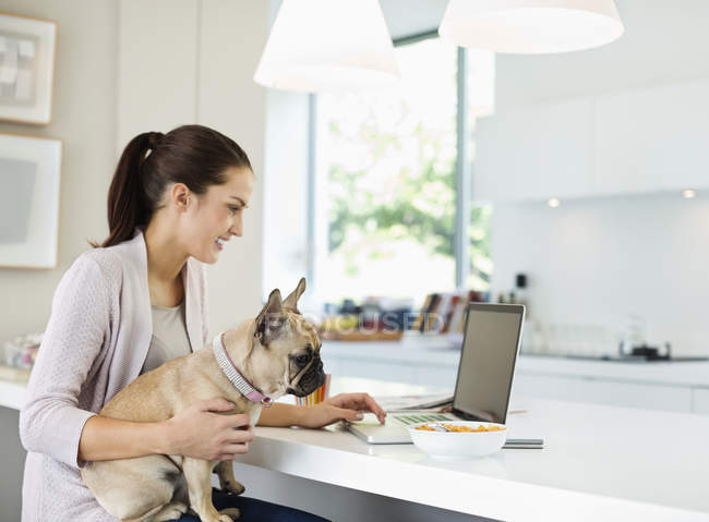 Frau benutzt Laptop mit Hund auf Schoß — Stockfoto
