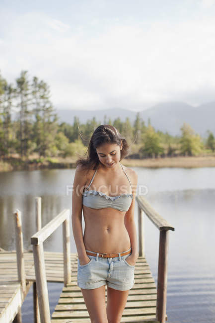 Woman looking down with hands in pockets on dock over lake — Stock Photo