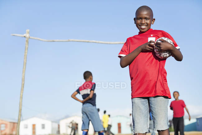 Африканський хлопчик тримає футбольний м'яч у ґрунтовому полі — стокове фото
