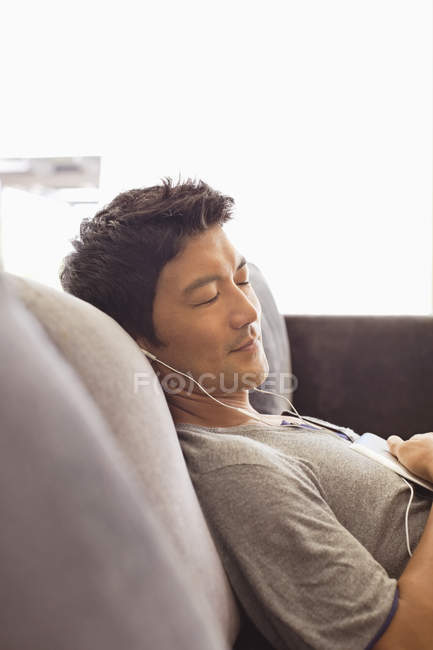 Молодой привлекательный мужчина слушает наушники на диване — стоковое фото