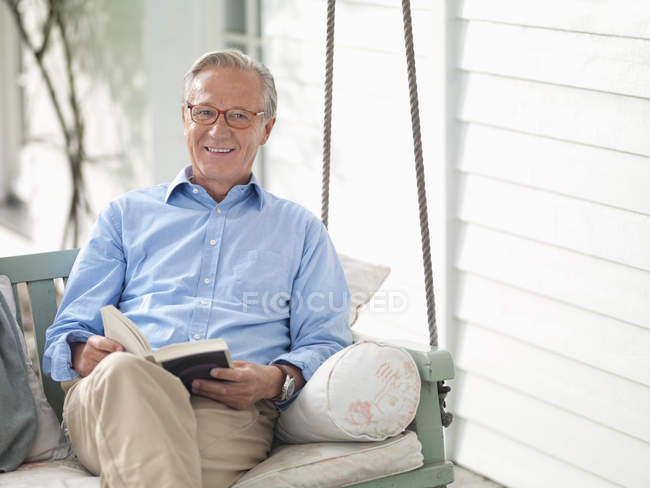 Hombre leyendo libro en columpio porche - foto de stock