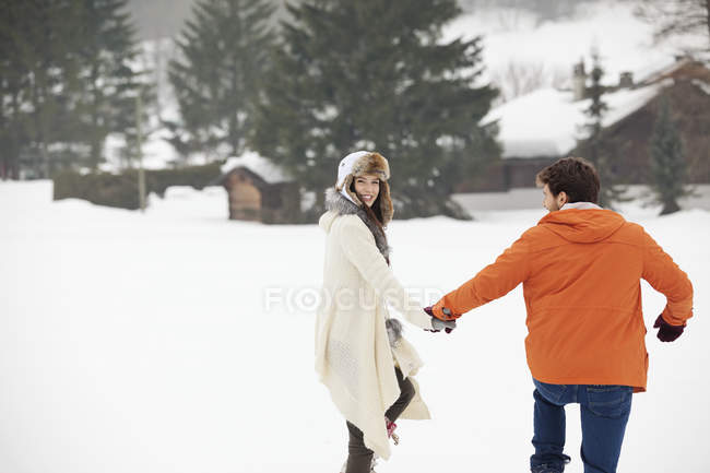 Happy couple holding hands and walking in snowy field — Stock Photo