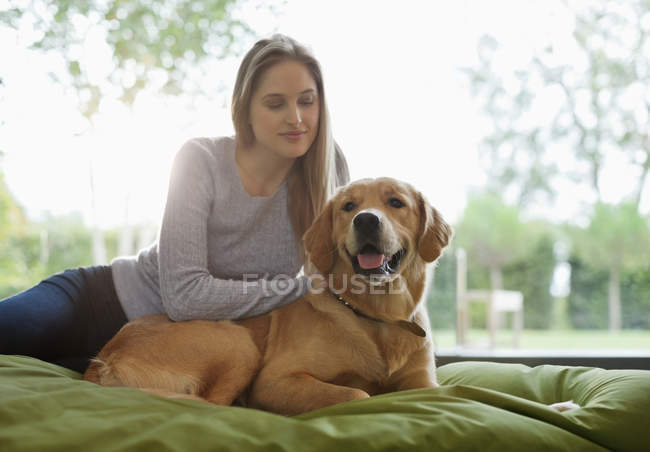 Mujer acariciando perro en la cama en casa moderna - foto de stock