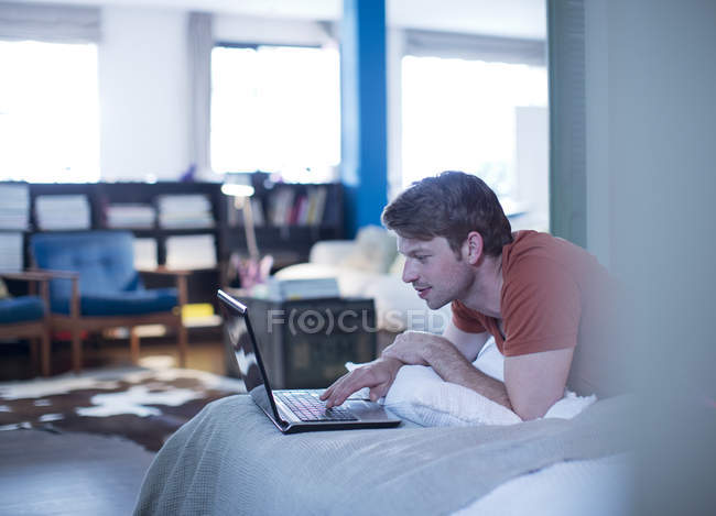Mann benutzt Laptop auf Bett — Stockfoto