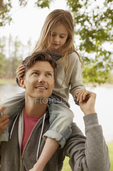 Father carrying daughter on shoulders at lakeside — Stock Photo