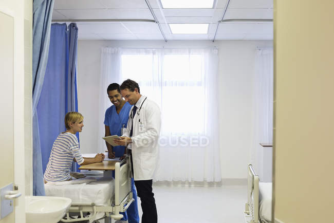 Médico y enfermera hablando con el paciente en la habitación del hospital - foto de stock
