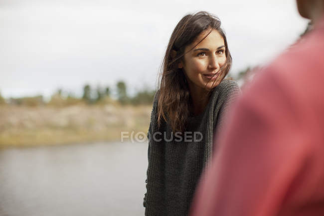 Mujer sonriente mirando al hombre a orillas del lago - foto de stock