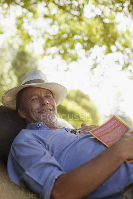 Retrato del hombre sonriente tendido en la hierba con libro - foto de stock
