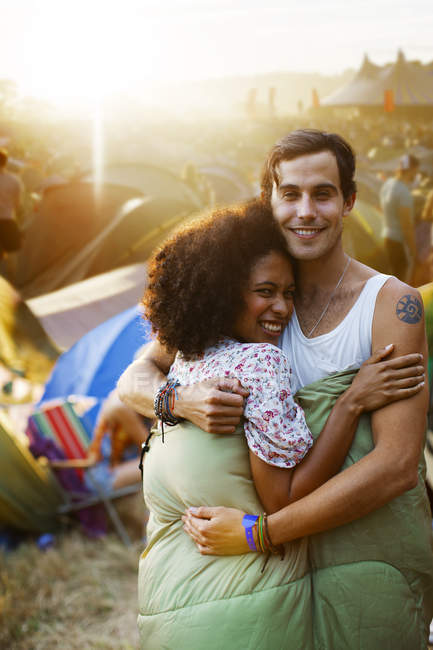 Couple in sleeping bag hugging outside tents at music festival — Stock Photo