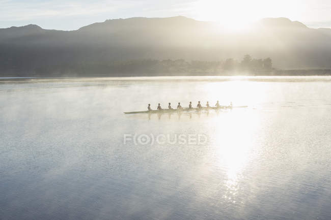 Rowing team rowing boat on still lake — Stock Photo