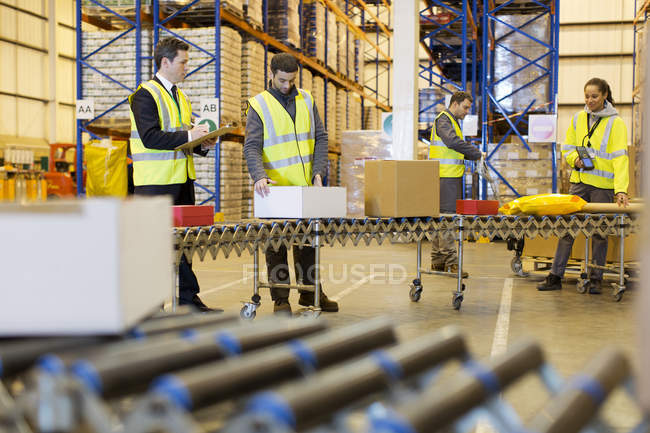 Trabalhadores que verificam as embalagens na correia transportadora no armazém — Fotografia de Stock