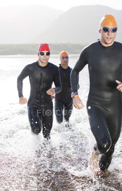 Triatletas confiantes e fortes em fatos de mergulho correndo em ondas — Fotografia de Stock