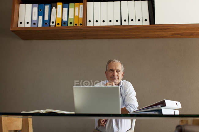 Hombre mayor sentado en el escritorio - foto de stock
