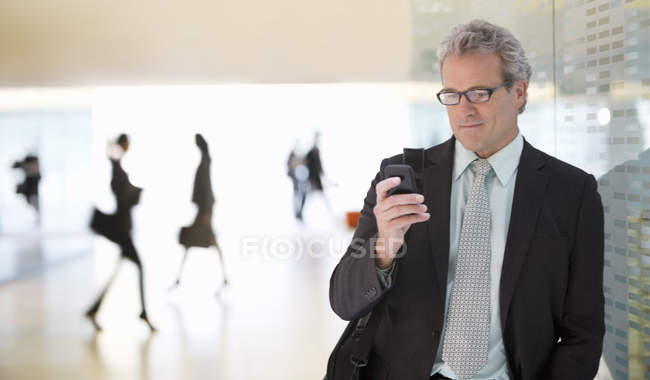 Mensagens de texto de empresário com telefone celular no lobby no escritório moderno — Fotografia de Stock