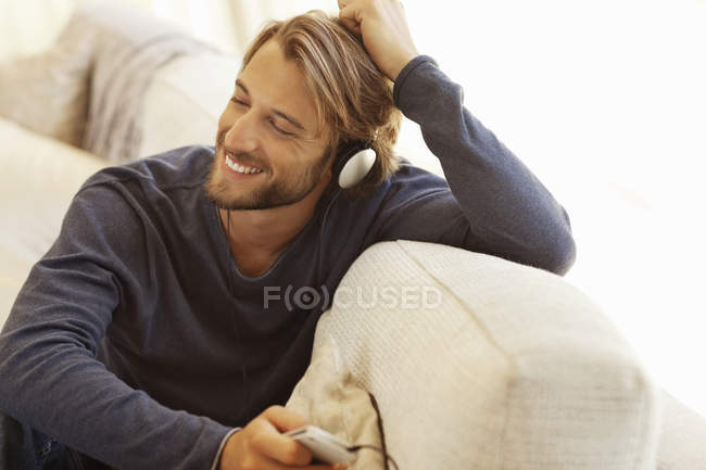 Jovem atraente Homem ouvindo fones de ouvido no sofá — Fotografia de Stock