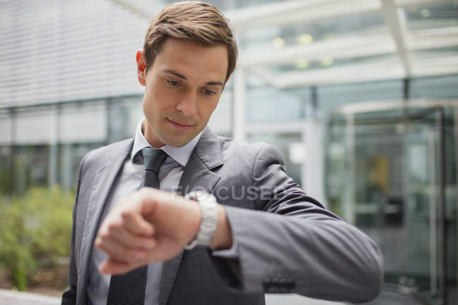 Бизнесмен смотрит на часы снаружи офисного здания — стоковое фото