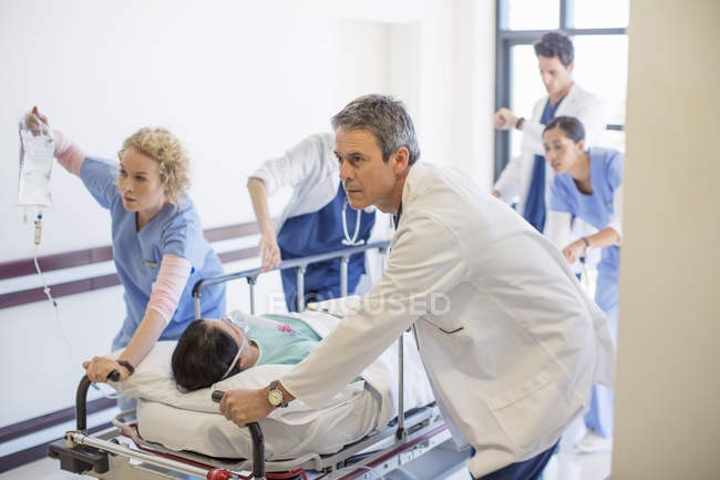 Doctors and nurses rushing patient on stretcher down hospital corridor — Stock Photo